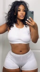 Busty woman in tight white shorts and crop top posing for a mirror selfie – adult phone chat UK profile image.