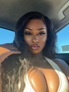 Busty black British woman with long black hair and seductive eyes sitting in a car, ideal for adult phone chat in London.