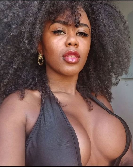 Curvy black woman with large natural afro curls wearing a low-cut top and bold lipstick, ideal for adult phone chat in Birmingham.