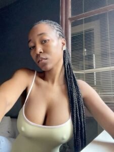 Braided Caribbean woman in a light top near window – seductive adult phone chat in Nottingham.