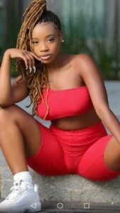 Beautiful Caribbean woman with blonde locs in a tight red outfit sitting confidently, perfect for adult phone chat in Manchester.