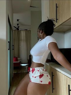 Curvy woman in white crop top and heart-print shorts leaning on kitchen counter, side pose – Romi Vibe, UK adult phone chat fantasy