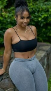 Curvy woman in grey leggings and black crop top smiling outdoors in Birmingham – adult phone chat model UK.