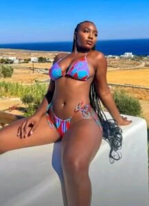 Curvy British Nigerian woman in a colourful bikini lounging outdoors with sea in the background – Zaria, adult voice chat queen in Brighton.