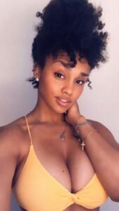 Busty Caribbean girl in yellow bikini top smiling—adult phone sex chat in Brighton UK.