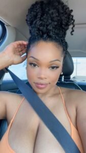 Curvy Caribbean woman with tied-up curly hair and deep cleavage in a car, wearing a low-cut top and a seductive look—adult phone chat in Bristol, UK.
