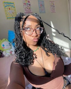 Busty girl with glasses and curly braids in low-cut top, making kissy face in bright room with plushies – Mochi Rae, UK nerdy adult chat girl