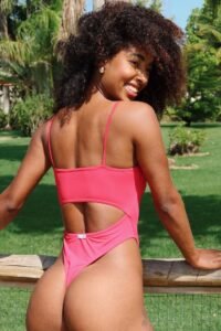 Curvy Caribbean woman in pink thong swimsuit, smiling flirtatiously outdoors – adult phone chat model in Brighton, UK.