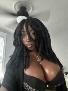 Busty Black woman with dreadlocks wearing black lingerie, intense gaze and gothic aesthetic, UK adult phone chat dominatrix – Nyomi Dusk