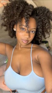 Busty girl with natural afro hair in baby blue top smiling softly — Zaria Monroe, Afro-Caribbean phone chat model in UK