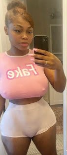 Curvy woman in pink crop top that says “fake” and white sheer shorts taking a mirror selfie – Trixie Starr, UK adult phone chat tease