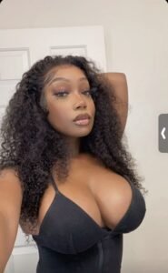 Curvy black woman with long curly hair and deep cleavage in black top—adult phone chat Birmingham UK.
