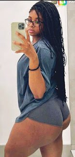 Mirror selfie of curvy Caribbean woman with long braids and glasses wearing a grey top and shorts – Kayla Storm, adult phone chat girl in UK