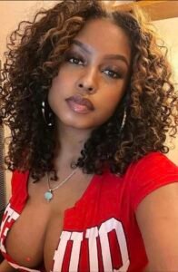 Busty woman with curly highlighted hair in red top posing seductively – UK adult phone chat profile.
