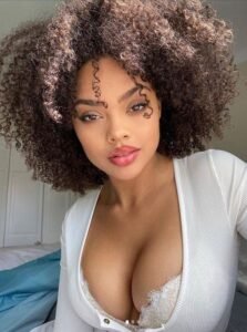 Beautiful woman with natural curls and plunging neckline posing in white top – adult phone chat Manchester UK profile.