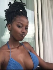 Beautiful Caribbean woman with dreadlocks and a flirty expression, wearing a blue bikini top, ideal for adult phone chat services in UK.