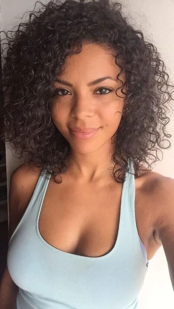 Curly-haired Caribbean woman in blue tank top smiling sweetly – adult phone chat in Birmingham.