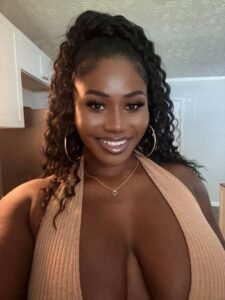 Naomi Blackwood – busty Caribbean woman with curly hair, smiling seductively in a low-cut top.