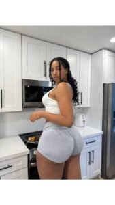 Isla Monroe – Curvy Caribbean woman in white tank top and grey shorts posing seductively in a modern kitchen in Leeds UK