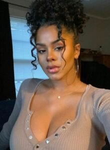 Curly-haired Caribbean model Sade Monroe in low-cut top offering sensual phone chat in the UK