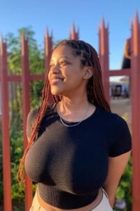 Busty Caribbean girl Malia Bliss smiling in tight black top for adult phone chat in the UK