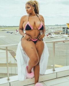 Jamaican beauty Layla Luxe in a black and pink bikini with a white cover-up, posing on a balcony overlooking an airport runway