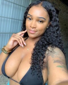 Caribbean beauty Serena Vale with long curly hair, wearing a black bikini top and smiling softly while taking a selfie