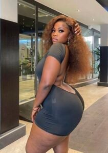 Caribbean beauty Nadia Fierce with golden brown curly hair, wearing a backless black dress and looking over her shoulder with a sultry expression.