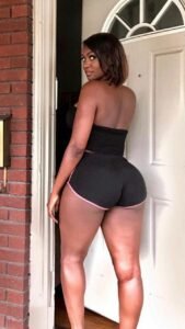 Sierra Monet – curvy Caribbean woman in black shorts, showing off her peachy figure at the doorway.