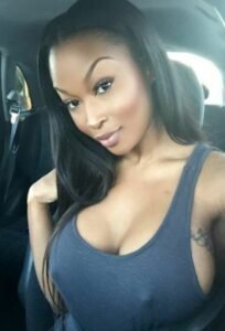 Caribbean beauty Zara Knight with long straight hair, wearing a grey tank top and smiling while sitting in a car