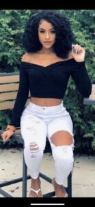 Tiana Rose, mixed-race woman with curly black hair, wearing a black off-shoulder top and ripped white jeans