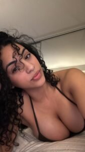 Caribbean beauty Alina Skye with curly hair, lying down in a bikini top, giving a soft and sultry look to the camera.