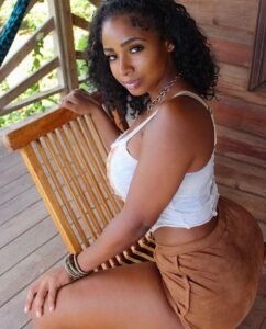 Serena Bliss – curvy Afro-Caribbean beauty sitting outdoors in a white top and brown skirt