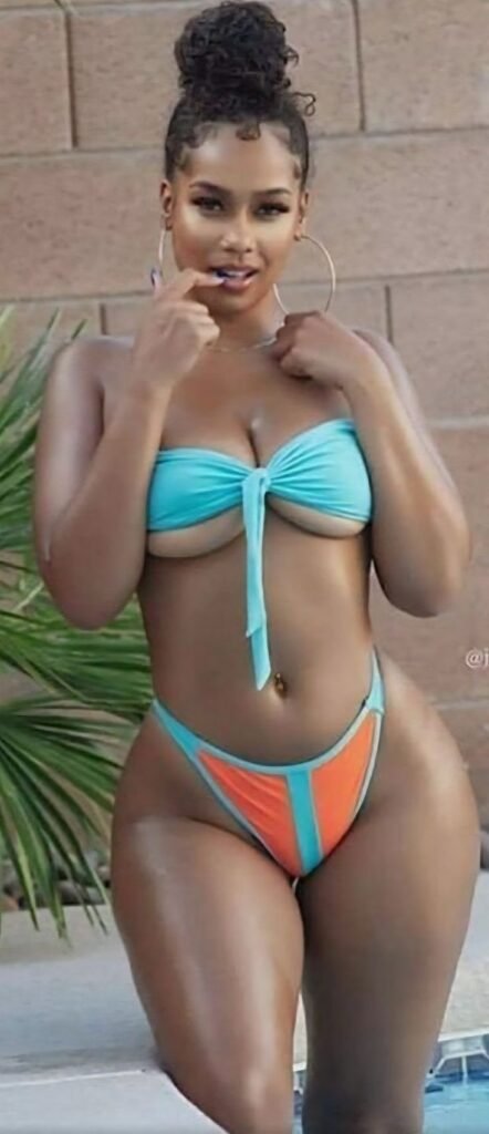 Saint Lucian beauty Selena Tide in a turquoise and orange bikini, posing confidently by the poolside with a flirty smile.