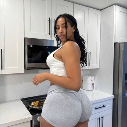 Isla Monroe – Curvy Caribbean woman in white tank top and grey shorts posing seductively in a modern kitchen in Leeds UK