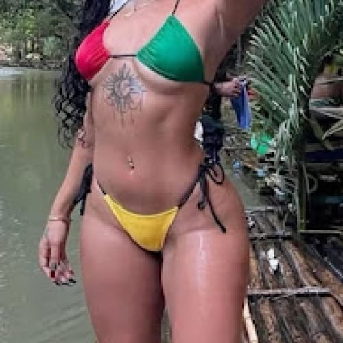 Curvy Jamaican woman in Rasta bikini posing by river, braided hair, tattooed belly, tropical fantasy adult chat model – Kiana Riddim, UK