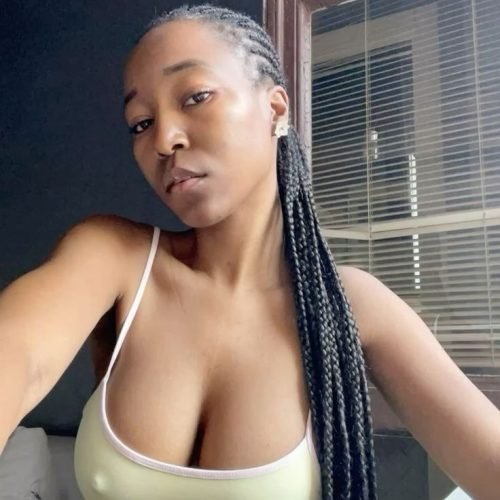 Braided Caribbean woman in a light top near window – seductive adult phone chat in Nottingham.
