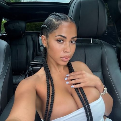 Caribbean beauty Amira Luxe with long braids in a white strapless top, sitting in a luxury car and giving a sultry look to the camera.