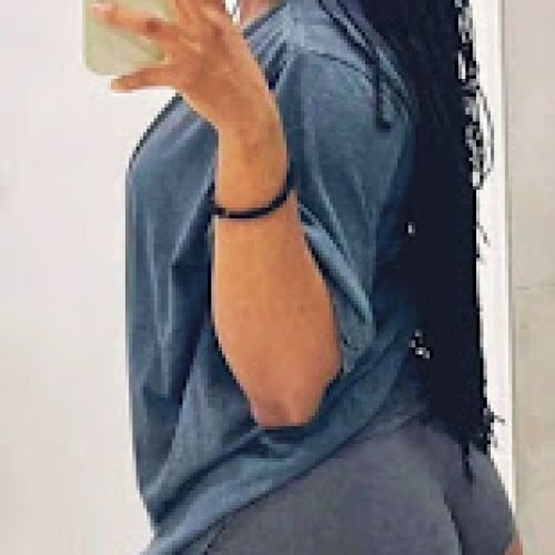 Mirror selfie of curvy Caribbean woman with long braids and glasses wearing a grey top and shorts – Kayla Storm, adult phone chat girl in UK