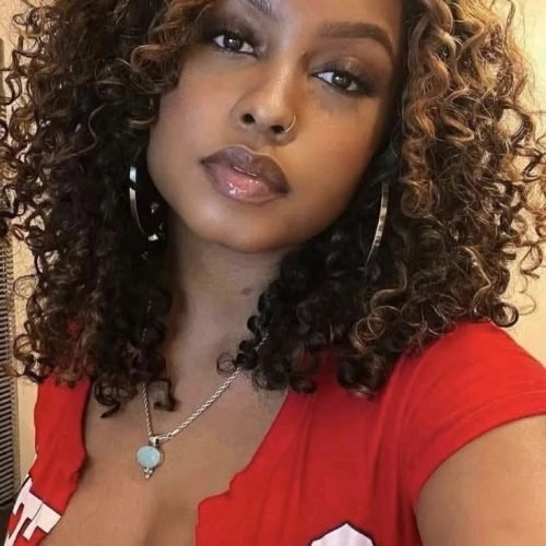 Busty woman with curly highlighted hair in red top posing seductively – UK adult phone chat profile.