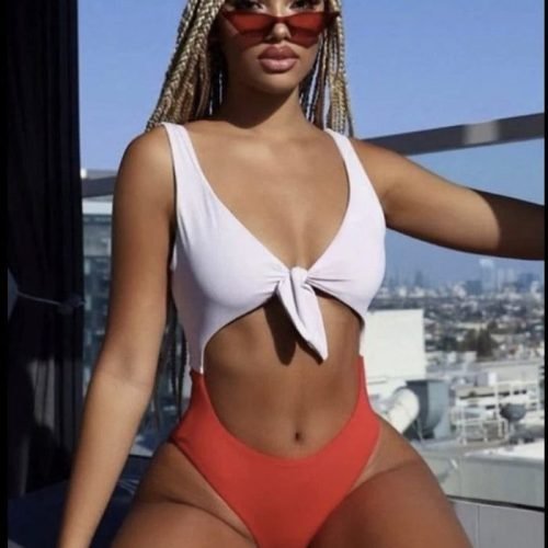 Light-skinned woman in a red and white swimsuit, braided hair and sunglasses, posing confidently on a rooftop in Manchester – adult phone chat model.