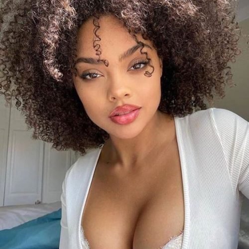 Beautiful woman with natural curls and plunging neckline posing in white top – adult phone chat Manchester UK profile.
